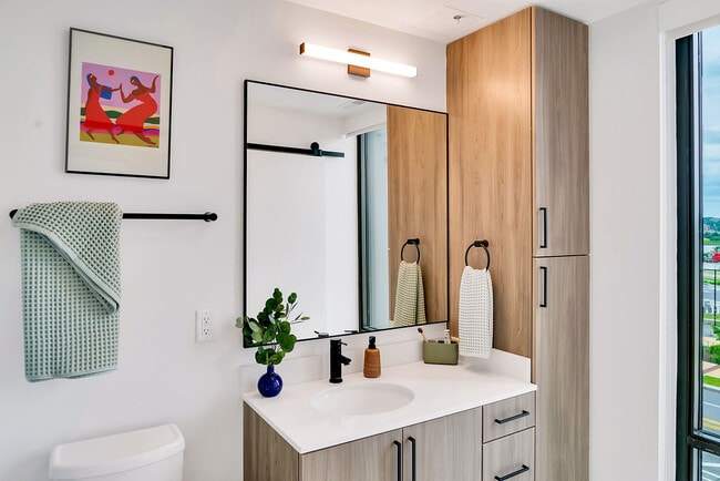 Modern bathroom with white walls, light wood cabinetry, large window, and decorative accents.