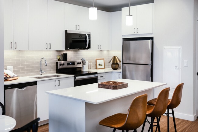 Design Collection I kitchen with stainless steel appliances, white cabinetry, grey tile backsplash, under-cabinet lighting, white quartz countertops, and hard surface flooring - Avalon Quincy Adams