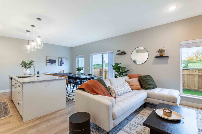 Modern living space featuring a cozy sectional sofa with elegant cushions, a sleek kitchen island with pendant lighting, and a spacious dining area opening to a scenic view. - Summerwell Maple Grove