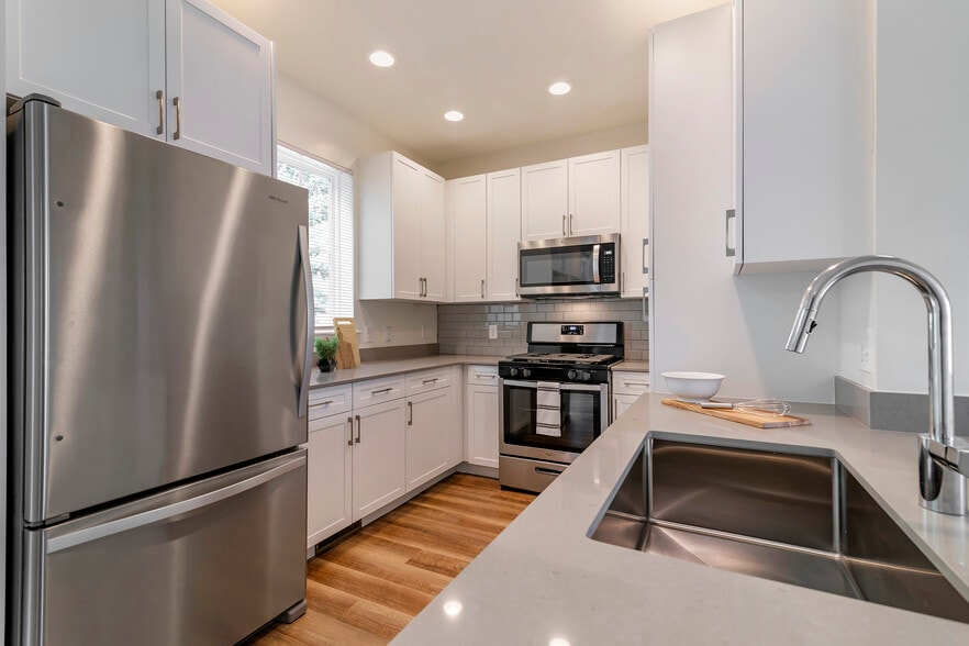 Renovated Package II kitchen with white cabinetry, grey quartz countertops,  grey subway tile backsplash, stainless steel appliances, and hard surface flooring
