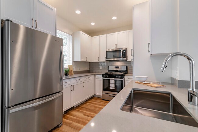 Renovated Package II kitchen with white cabinetry, grey quartz countertops, grey subway tile backsplash, stainless steel appliances, and hard surface flooring - Avalon Northborough Apartments