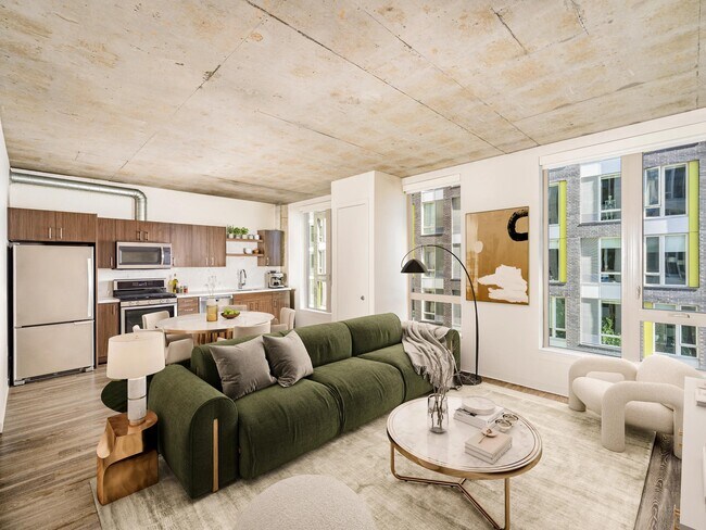 An open apartment home with concrete ceilings, expansive windows, and a streamlined kitchen, offering flexible living space filled with natural light. - Modera Pearl