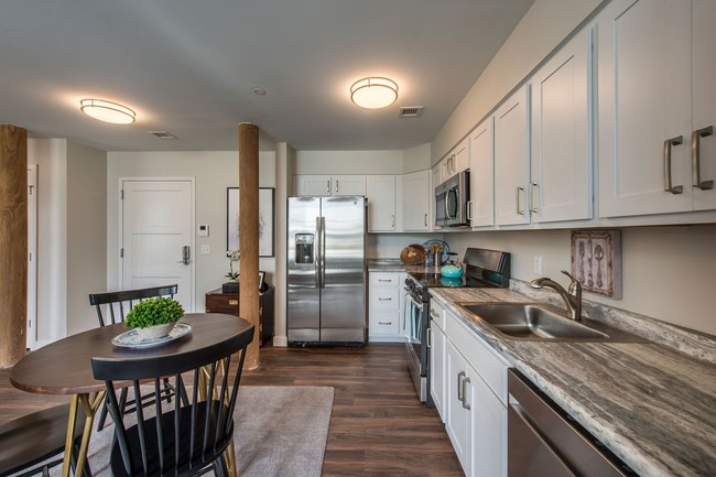 Kitchen And Dining Room With Faux Quartz Counters, White Cabinets, Stainless Appliances, Wood Plank. - Sterling Lofts, A 55+ Community