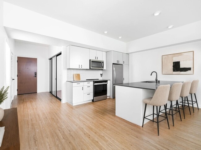Kitchen with quartz countertops, bar seating, and streamlined cabinetry opening to a bright living area with natural light and clean finishes.