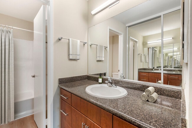 Renovated Package I bath with grey speckled granite countertops, chestnut cabinetry, and hard surface flooring