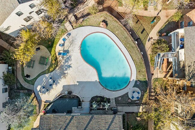 Aerial view of freeform community swimming pool surrounded by concrete deck, lounge chairs, and mature trees