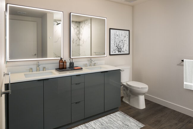 Upgrade Package Bath with grey cabinetry, white quartz countertop, marble shower surround, and lit vanity mirror
