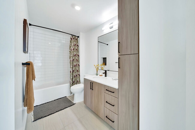 Modern bathroom with white walls, light wood cabinetry, large window, and decorative accents.