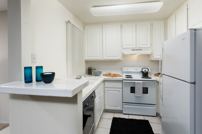 Classic kitchen with white tile countertops, white cabinetry, white appliances, and tile flooring - eaves Warner Center Apartments