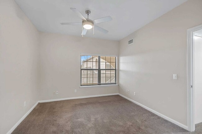 Spacious bedroom with carpet flooring, ceiling fan, large window, neutral walls, and open doorway leading to adjacent room