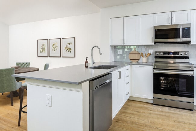 Renovated Package III kitchen with stainless steel appliances, grey quartz countertops (select homes), white cabinetry, light grey tile backsplash, and hard surface flooring - eaves West Windsor Apartments