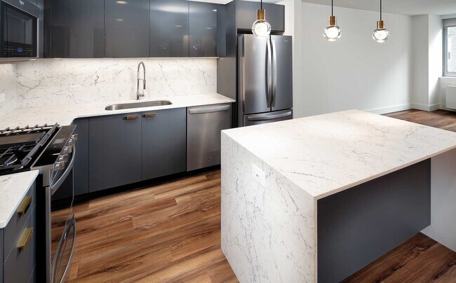 Signature Collection kitchen with pendant lighting, quartz stone countertop with waterfall edge, cabinetry with matte and high gloss finish, and SMART stainless steel appliances