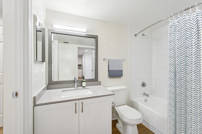 Baño renovado del Paquete II con gabinetes blancos, encimeras de cuarzo gris y pisos de superficie dura.