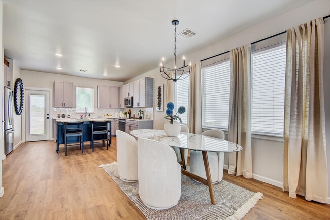 Open dining area with round table, upholstered chairs, chandelier, and kitchen with island seating