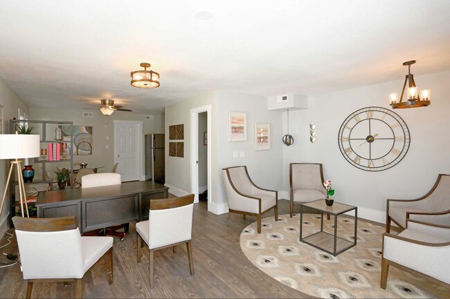 Open-plan living and dining space with hardwood floors, accent chairs, large wall clock, and gold pendant lighting