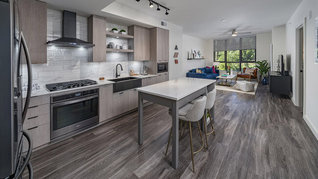 Apartment kitchen with stainless steel appliances, dining and living room with wood-style flooring. - Griffis Edgemoor Apartments