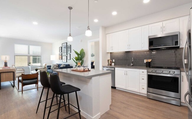 Upgrade Collection kitchen and dining area with stainless steel appliances, white cabinetry, grey quartz countertop, grey tile backsplash, and hard surface flooring
