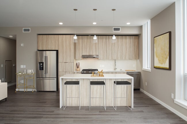 Signature Collection penthouse kitchen with oak cabinetry and undercabinet lighting, white quartz countertops and backsplash, upgraded stainless steel appliances, and hard surface flooring.