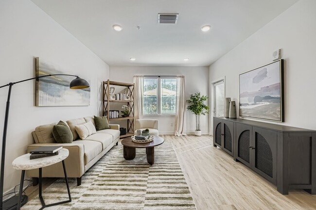 Bright and modern living room featuring a cozy beige sofa, stylish artwork, and abundant natural light from large windows.