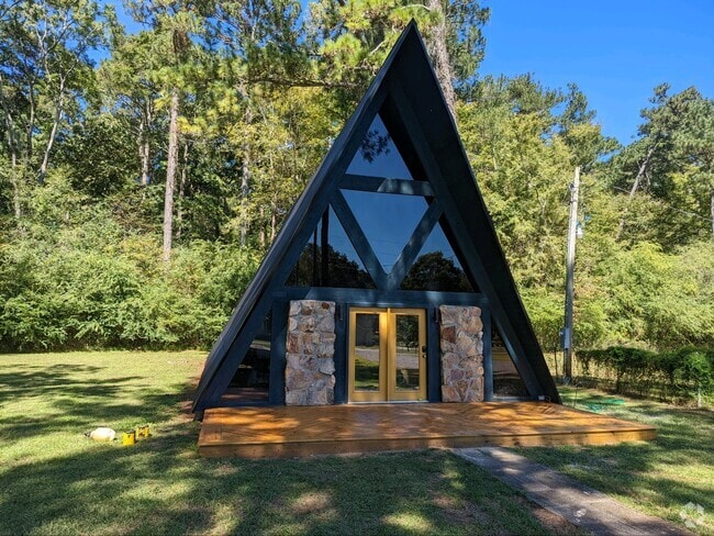 A modern A-frame cabin with a stone entryway, large glass windows, and a peaceful wooded backdrop. - 2406 Crockett Cir Rental