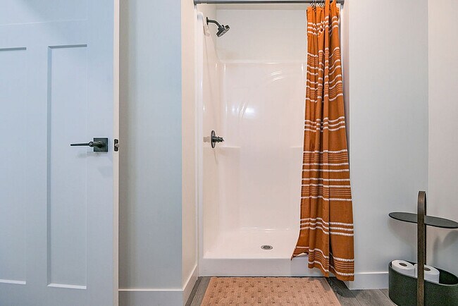 Modern bathroom featuring a sleek shower with an elegant orange stripe curtain, complemented by a stylish storage shelf and a contemporary door design. - Orchard on Wallen