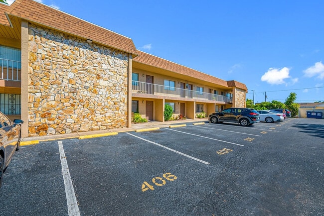 Inviting two-story apartment complex with stone facade, ample parking, and lush greenery under a clear blue sky.