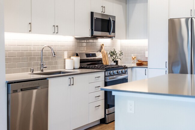 Kitchen with grey quartz countertops, white cabinetry, grey subway tile backsplash, stainless steel appliances, and hard surface flooring