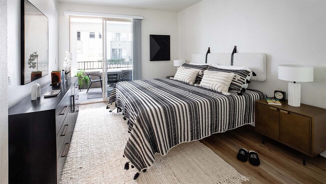 Spacious apartment bedroom with wood-style flooring and balcony access. - Griffis Mission Valley