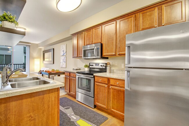 An open kitchen with stainless steel appliances and shelving with a view through to the living area - The Artiste Apartments