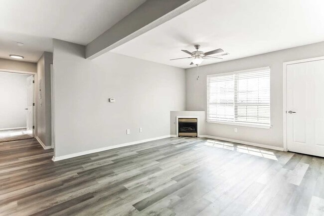 Living room with wood style flooring, fireplace, ceiling fan, large window, and open hallway leading to bedroom areas