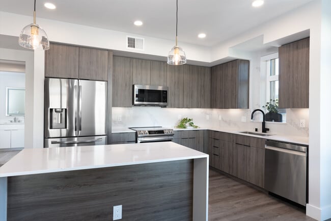 Signature Collection Kitchen with wood cabinetry, marbled quartz countertop and backsplash, upgraded stainless steel appliances, and hard surface flooring - Avalon West Dublin Apartments