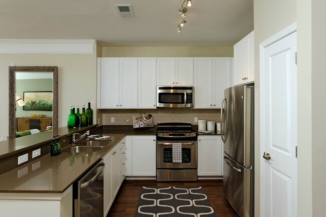 Kitchen with quartz stone countertop, white cabinetry, tile backsplash, stainless steel appliances and hard surface flooring