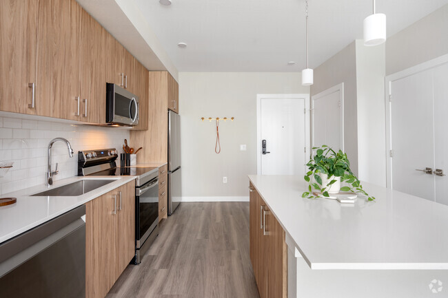 Finish Package II Kitchen with oak cabinetry, white quartz countertops, stainless steel appliances, pendant lighting, and hard-surface vinyl plank flooring - Avalon Westminster Promenade Rental