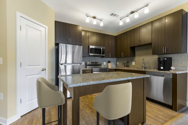 Upgraded kitchen with espresso cabinetry, grey speckled granite countertops, light grey tile backsplash, stainless steel appliances, and hard surface flooring