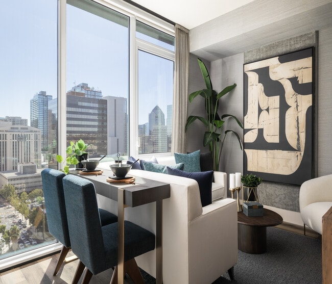 Modern apartment interior with elegant dining area, plush seating, and panoramic city views through large windows.
