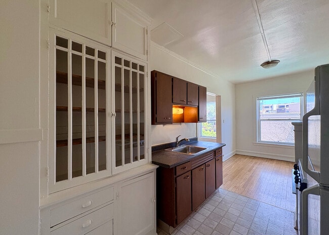 Bright and inviting kitchen with sleek wooden cabinets, a large window for natural light, and classic built-in shelving, offering a perfect blend of style and functionality.