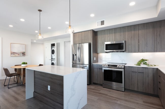 Signature Collection Kitchen with wood cabinetry, marbled quartz countertop and backsplash, upgraded stainless steel appliances, and hard surface flooring