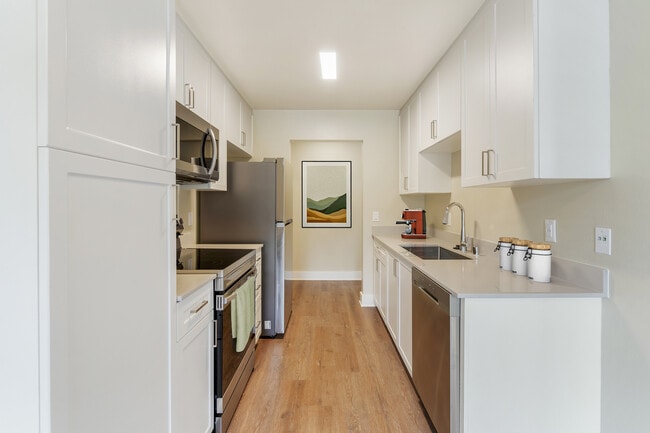 Renovated Package I kitchen with beige granite countertops, white cabinetry, stainless steel appliances, and hard surface flooring
