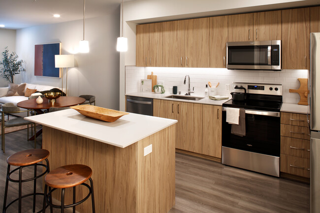 Design Collection II Kitchen with oak cabinetry, white quartz countertops, and white tile backsplash - Avalon Alderwood Place Apartments