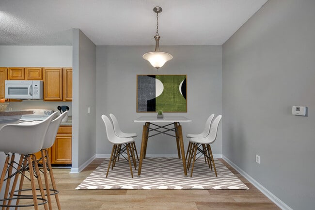 Living room and kitchen view at Dunwoody Place showcasing an open floor plan with light wood floors, modern furnishings, bar-height counter seating, and natural light in an affordable apartment home in Huntsville, AL. - Dunwoody Place