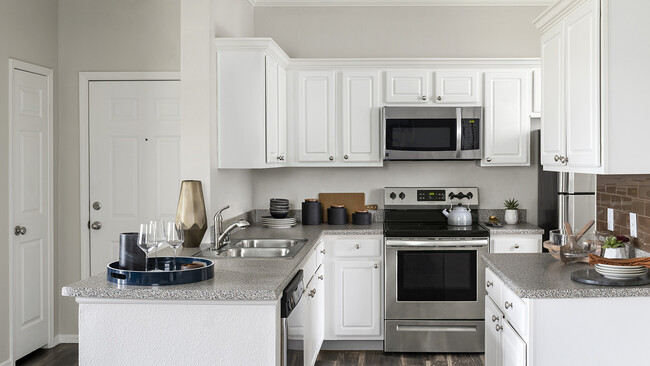 Cocina del apartamento con electrodomésticos de acero inoxidable, encimeras de granito y pisos de madera. - Sagebrook Apartamentos