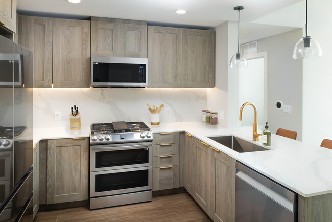 Signature Collection kitchen with stainless steel appliances, marbled white quartz countertops, brown cabinetry, and hard surface flooring - Avalon Montville Apartments