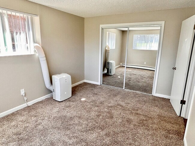 Dormitorio luminoso con alfombra de felpa, puertas de armario con espejos y aire acondicionado portátil moderno para mayor comodidad y estilo.