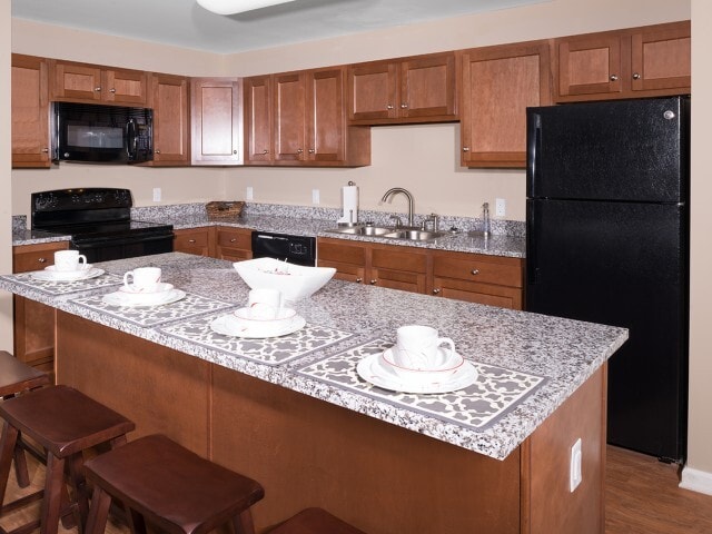 Enhance your student living with cherry wood cabinets, granite countertops, and sleek black appliances at University Hills Apartments - University Hills Apartments