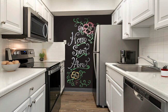 Renovated Package I kitchen with white cabinetry, laminate countertops, new stainless steel appliances, chalkboard accent wall, and hard surface flooring - AVA Van Ness