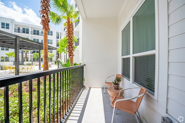 Charming apartment balcony with modern chairs, table, and lush garden view featuring palm trees and vibrant greenery.