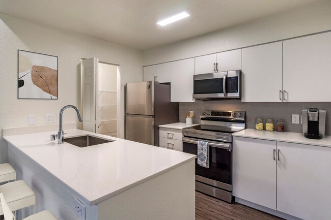 Paquete renovado I cocina con electrodomésticos de acero inoxidable, crema de encimeras de cuarzo, gabinetes de color blanco, placa para salpicaduras de azulejos gris, y pisos de superficie dura.