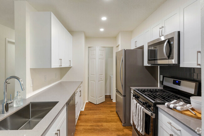 Renovated Package I kitchen with white cabinetry, grey quartz countertops, glass tile backsplash, and stainless steel appliances, and hard surface plank flooring - Avalon at Lexington Rental