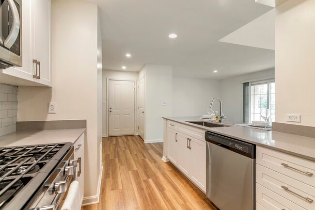 Renovated Package I kitchen with white cabinetry, grey quartz countertops, grey tile backsplash, stainless steel appliances, and hard surface plank flooring - Avalon at The Pinehills