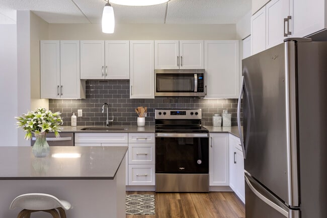 Renovated Package II kitchen with grey quartz countertops, white shaker cabinetry, stainless steel appliances, grey tile backsplash, and hard surface flooring throughout